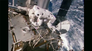 Kate Rubins au travail sur l'ISS, avec la capsule Dragon en arrière plan. Crédit : NASA TV